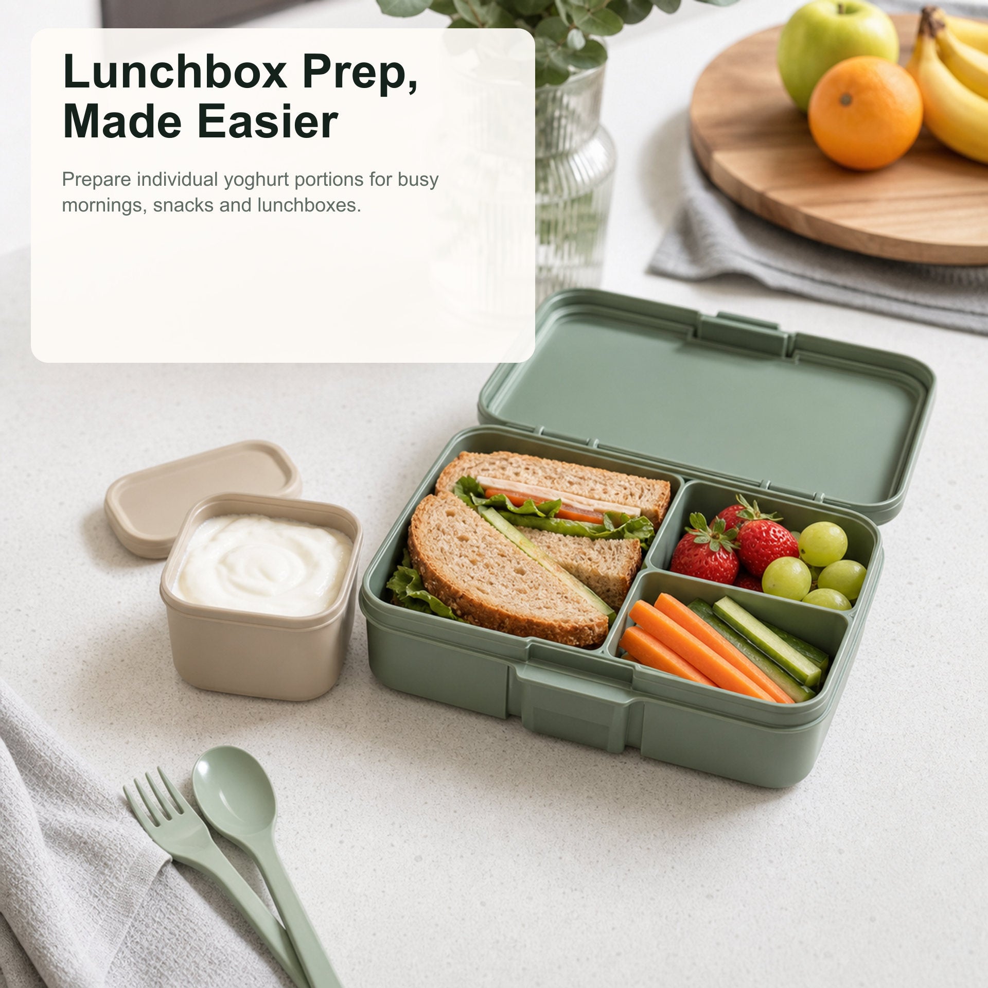Green bento box with a sandwich, fruits, and vegetables on a white tablecloth.