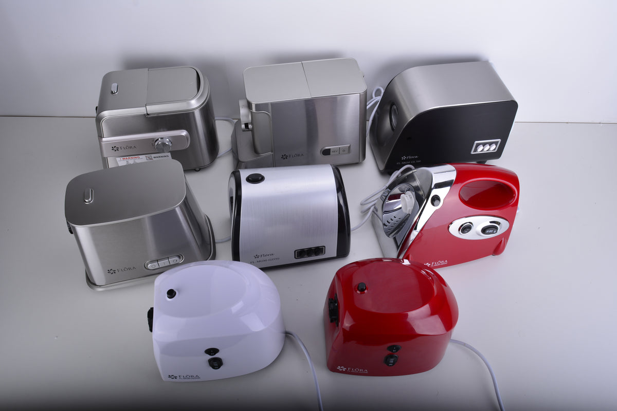A group of small countertop kitchen appliances photographed on a light gray surface against a light gray background. The set includes several toaster-style devices in silver, black, white, and red, along with a metallic iron and a red electric kettle or tea maker.