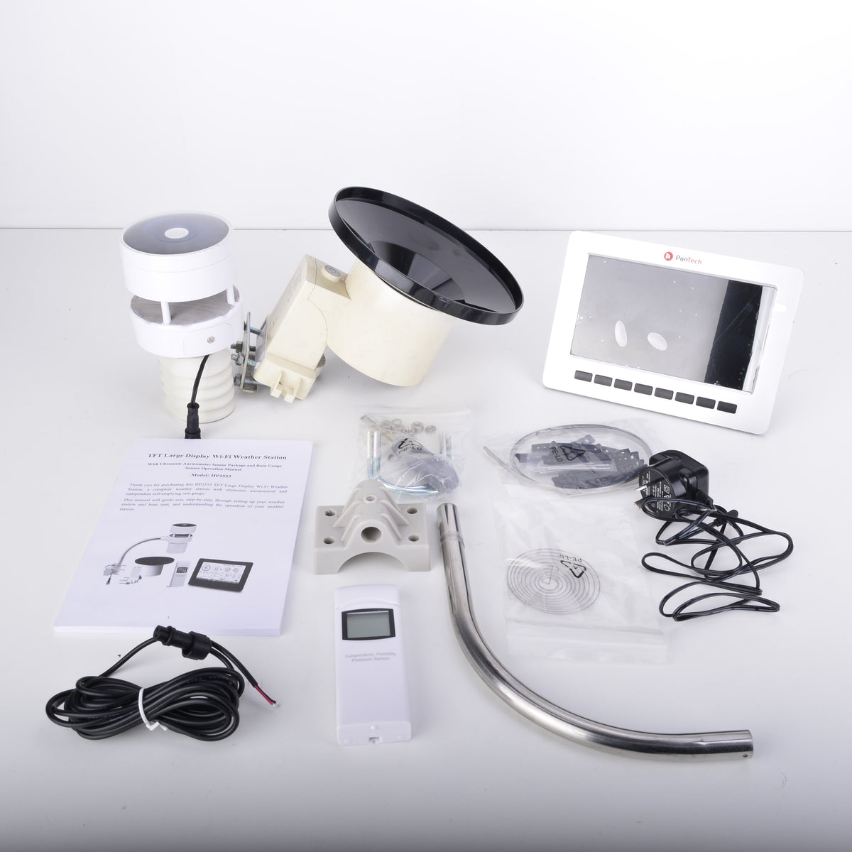 A complete outdoor security camera kit laid out on a white surface, including a white and black dome camera, a white mounting bracket, a curved metal pipe, a white control box, a white screen, a power adapter, cables, and an instruction manual.